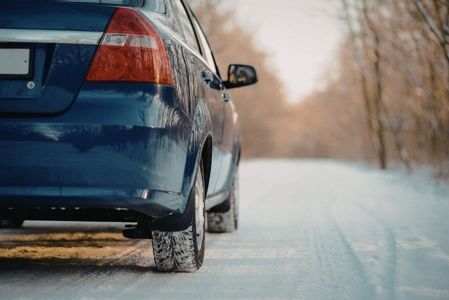 Blue car driving on snow covered road in winter